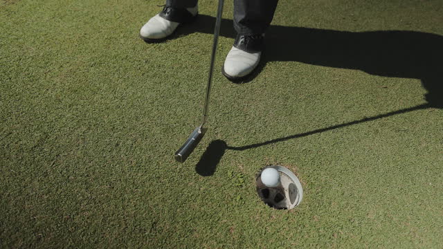 Skilled golf player putting ball into hole on green