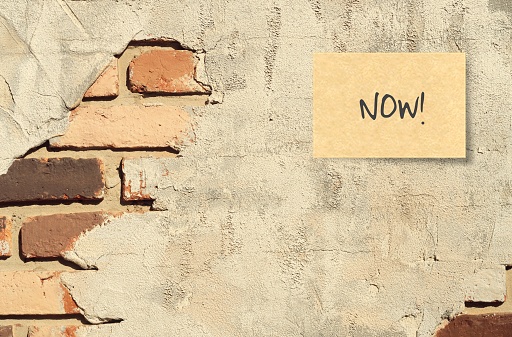 A handwritten text message on ruined cracked brick wall background : Now! , concept of Living in present /doing right now, no procrastination anymore