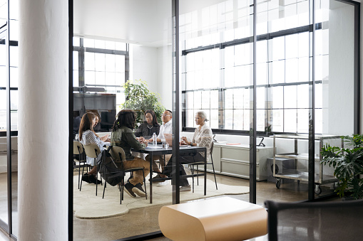 Diverse group sitting around conference table in modern office and developing project plans.