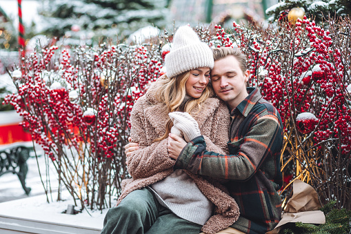 Portrait of young loving happy beautiful couple having fun enjoying decorated Xmas market. Kiss, hug, embrace each other, precious magic moments together on holiday time. Warm clothes, snow