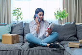 Young woman sitting at home unpacking cardboard box with online shopping