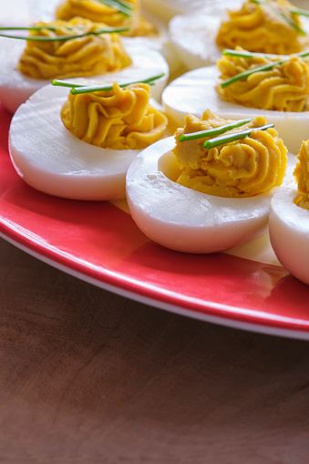 Closeup of stuffed eggs with two sprigs of chives on a plate with a red edge on a wooden table. Image with copy space.