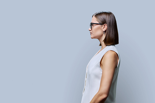 Profile view, confident successful serious young business woman wearing glasses, copy space gray studio background space for advertising image text. Business, work, services, education, people concept