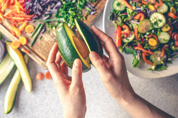 istock Avocado in female hands on a background of vegetables on the kitchen table. 1902059326