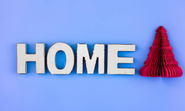 The word Home from wooden letters and a paper Christmas tree on a blue background.