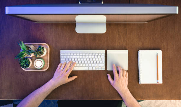 istock A man works at a computer, top view. Desktop computer on a wooden table. 1902064725