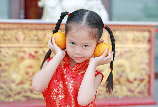 Cute asian kid girl in Traditional Chinese dress with holding sacred Orange at chinese temple in bangkok thailand, Chinese new year concept.