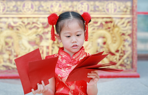 Happy little Asian child girl holding many red envelopes during Chinese new year festival.