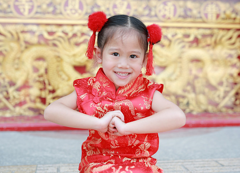 Happy little Asian child girl wearing red cheongsam with greeting gesture celebration for Chinese New Year at chinese temple in thailand.