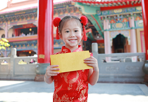 Happy little Asian child girl holding gold and red envelope on white background during chinese new year festival.