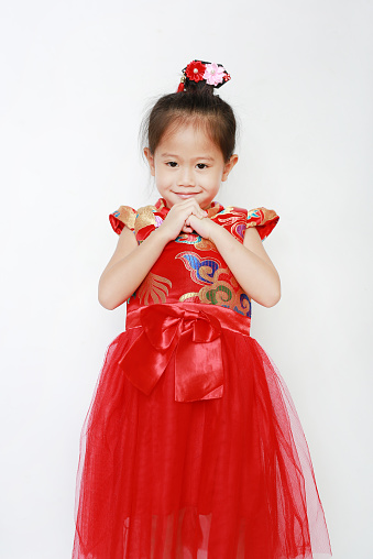 Happy little Asian child girl wearing red cheongsam with greeting gesture celebration for Chinese New Year isolated on white background.