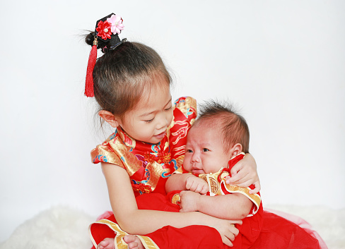 Adorable little asian girl and infant baby boy in cheongsam isolated on white background during traditional chinese new year festival.