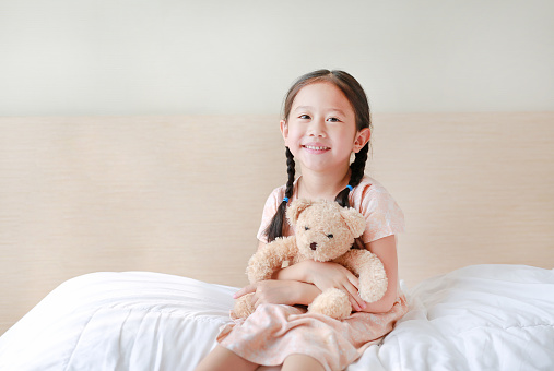 Girl (8-9) holding teddy bear, smiling, portrait