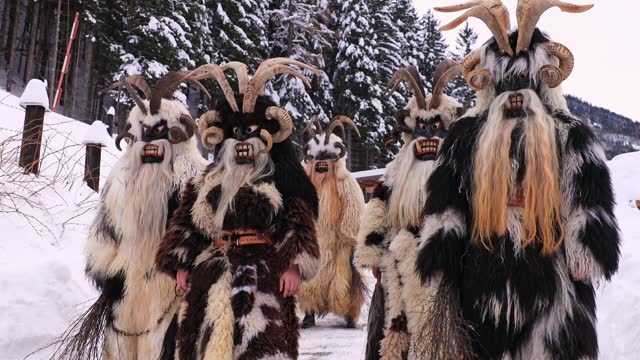 A group of Krampus stands against the backdrop of a village mountain road, Austria