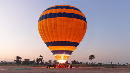 Hot air balloon is inflating before liftoff - Hatshepsut Temple at sunrise in Valley of the Kings and red cliffs western bank of Nile river- Luxor- Egypt