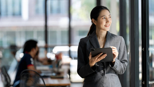 istock Smiling confident business leader standing in an office at team meeting. Using digital tablet during a meeting. 1902154104