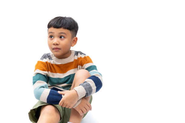 front view of  boy dressed in sportswear sitting on the floor looking at camera on a white background