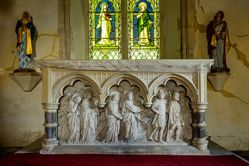 Interior of All Saints Church, Hulcott, showing carved altar, religious icons and partial stain-glass window.