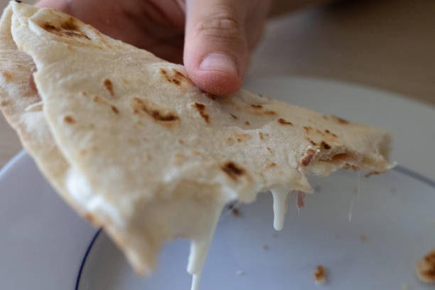 istock Hand Holding a Bitten Flat Bread Filled with Cheese and Ham on top of a Plate 1902178364