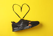 Black sports sneaker with heart-shaped laces on yellow background