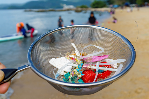 The close-up image of a volunteer wearing glove and using colander to clear away plastic pieces and rubbish on the beach. Volunteers play a crucial role in helping to reduce the impact of plastic pollution on coastal ecosystems.