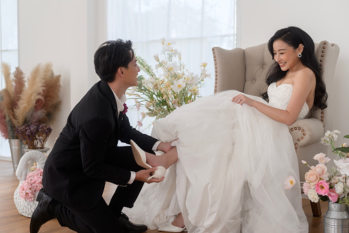 Groom helping and putting on elegant shoes for beautiful bride on ceremony wedding day