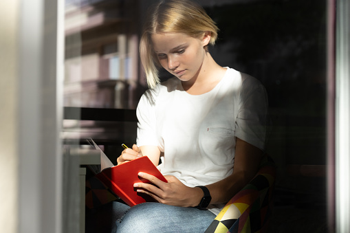 girl in a white shirt thinking about what to write down plans and wishing for the coming year in a red notebook