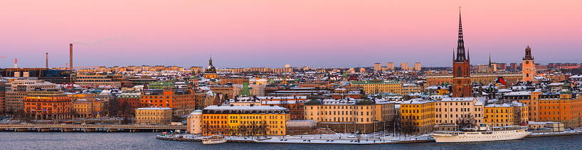 A colorful panoramic photo of Stockholm with the old town, the historic buildings of Riddarholmen, the old german church, roof of the royal palace and downtown Stockholm covered in winter snow.