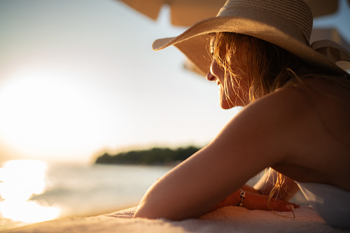 Close-up of a woman whit sun hat lying at the beach during sunset