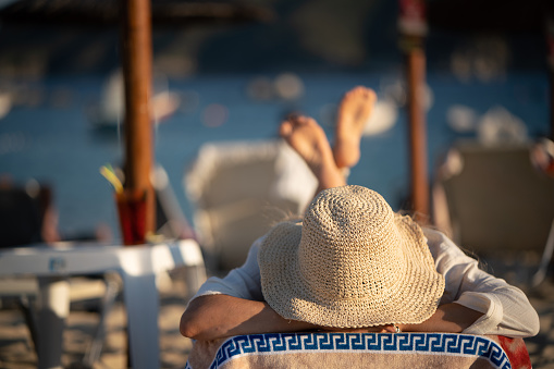 Unrecognizable woman whit sun hat lying on deck chair at the beach