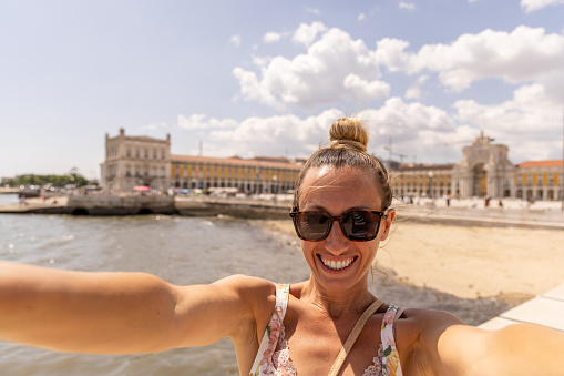 Tourist in Lisbon taking selfie, she smiles at the camera, sunny beautiful day. Staycation in Europe