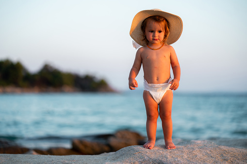 Full length of a little girl whit sun hat standing on the rock at the beach