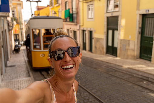 Tourist in Lisbon taking selfie, she smiles at the camera, sunny beautiful day. Staycation in Europe