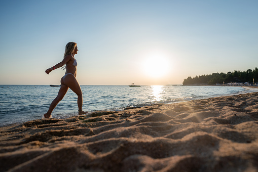 Full length of a happy woman in bikini walking at the beach. Copy space