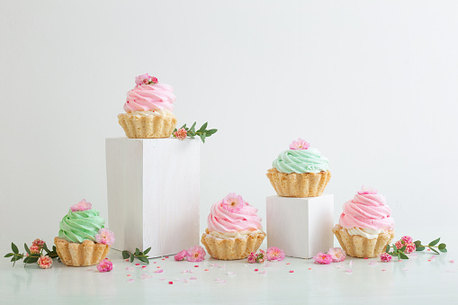 pink and green cupcakes with spring flowers  on wooden podiums on white  background