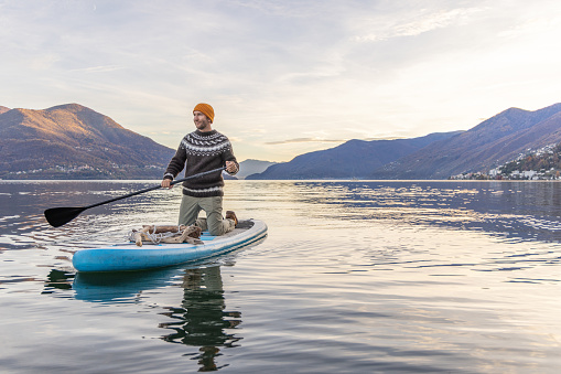 Weekend activity, people spending time outdoors enjoying nature. Man paddles on a stand up board on a calm lake in Switzerland