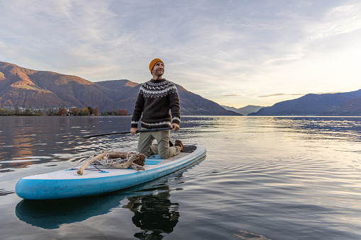 Weekend activity, people spending time outdoors enjoying nature. Man paddles on a stand up board on a calm lake in Switzerland