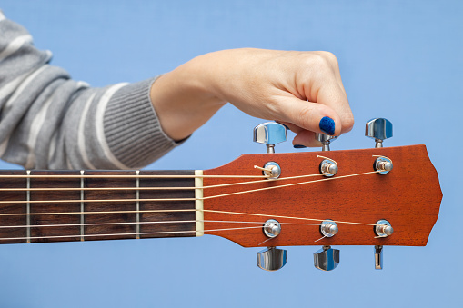 woman tuning an acoustic guitar, shot close-up. fingers rotate the guitar peg