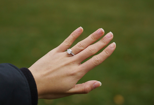 Young woman's hand with diamond engagement ring over green background