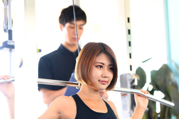 istock A young Asian woman doing lat pulldown weight training at the gym and a male personal trainer watching her. 1902583542