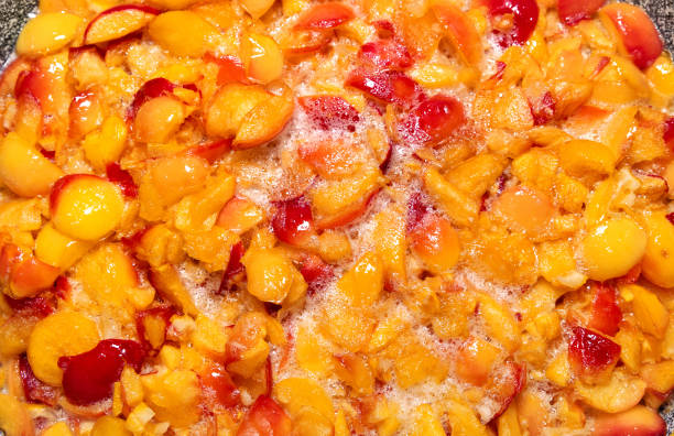 Making apple jam. Fresh chopped red and yellow apples in a saucepan in sugar syrup. Fruit sugar background.