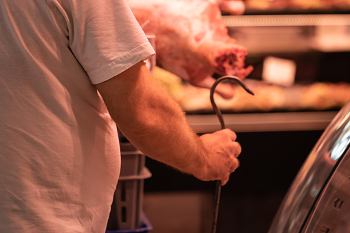 Unrecognizable butcher working with a hook in his hand in the marketplace