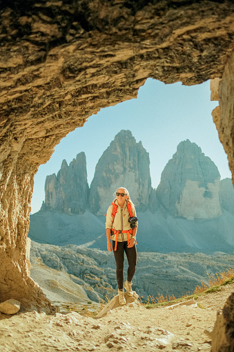 Young woman backpacker hikes in archway of mountain, spires behind