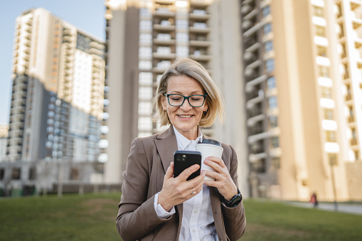 woman stand in front of a building with coffee to go use mobile phone