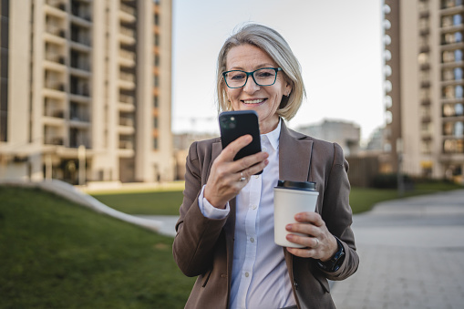 woman stand in front of a building with coffee to go use mobile phone