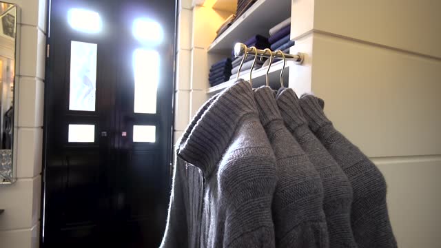 Panning over several men's gray sweaters on hangers in a men's clothing store