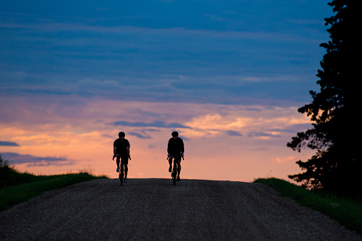 Two men go for an early morning gravel bike ride on a country road near Calgary, Alberta, Canada, in the summertime. Gravel bikes are like road bikes but with sturdy wheels and tires for riding on rough terrain.