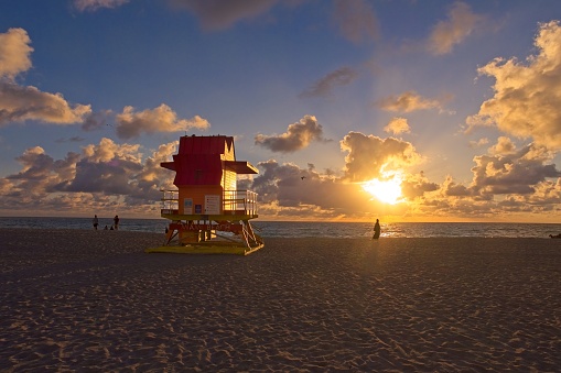 Morning sun breaks on South Beach Miami with tourist silhouette and life guard shack.