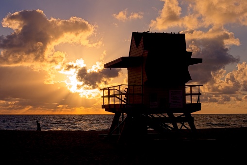 The orange sun glow of a Miami sunrise against the silhouette of a lifeguard beach hut.