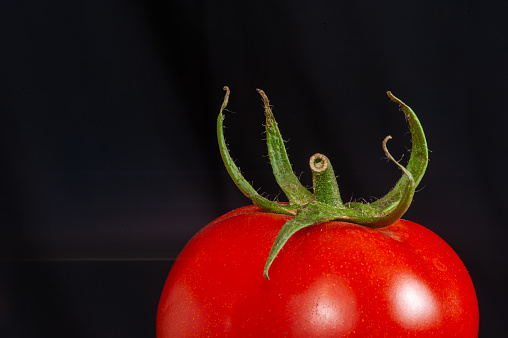 A unique tomato with deep fleshy folds, photographed on a black wooden background in dramatic light.